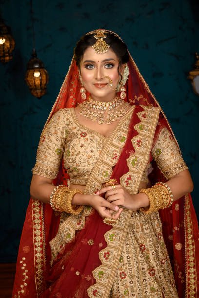 Stunning Indian bride dressed in traditional bridal lehenga with heavy gold jewellery and veil posing fashionable in studio lighting. Wedding fashion and lifestyle.